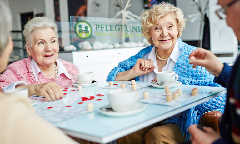 Ältere Damen lachen beim Brettspiel mit weißem Haar und bunter Kleidung.