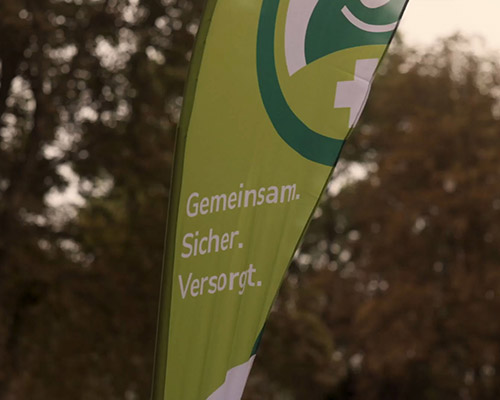 Grünes Banner mit Logo, weißer Schrift: "Gemeinsam. Sicher. Versorgt."
