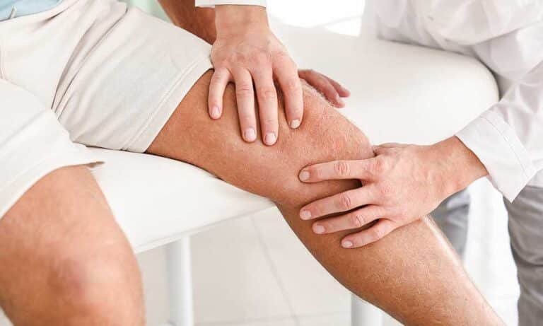 Zwei Personen untersuchen ein Knie auf einer medizinischen Liege.
