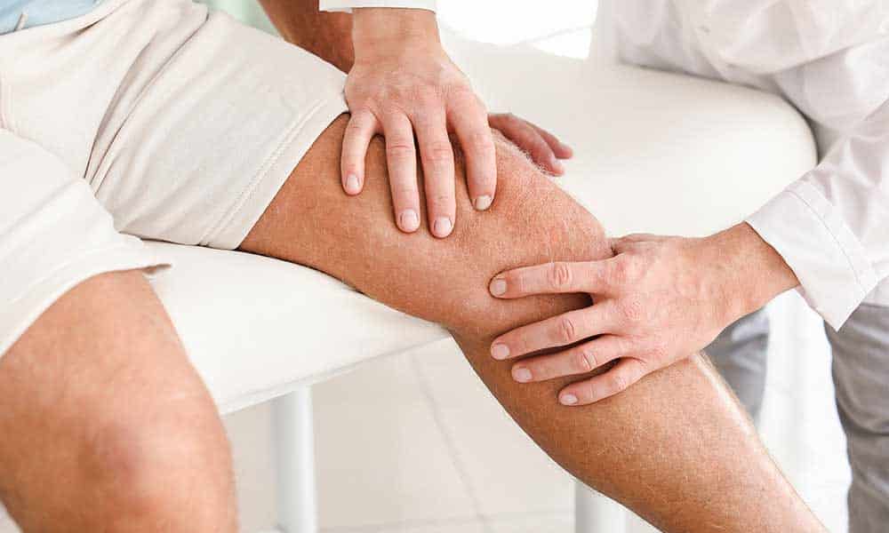 Zwei Personen untersuchen ein Knie auf einer medizinischen Liege.