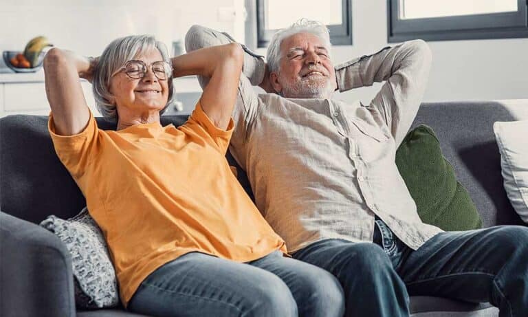 Ein älteres Paar sitzt entspannt auf dem Sofa, lächelnd und zufrieden.