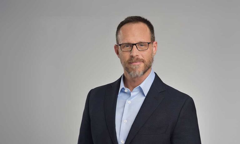 Ein Mann im Anzug mit Brille lächelt leicht und sieht professionell aus