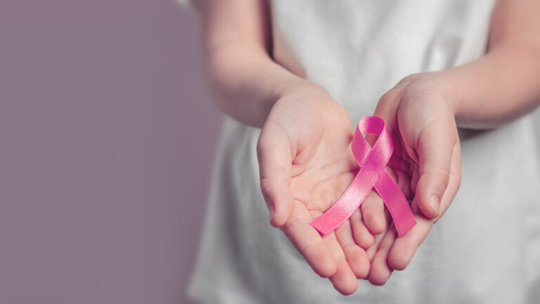 Eine Person hält ein rosa Band für Brustkrebsaufklärung in offenen Händen