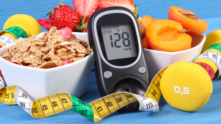 Blutzuckermessgerät zeigt 128 mit Schalen Müsli Obst gelbem Ball und Maßband