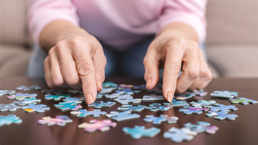 Eine ältere Person sortiert bunte Puzzleteile auf einem Tisch