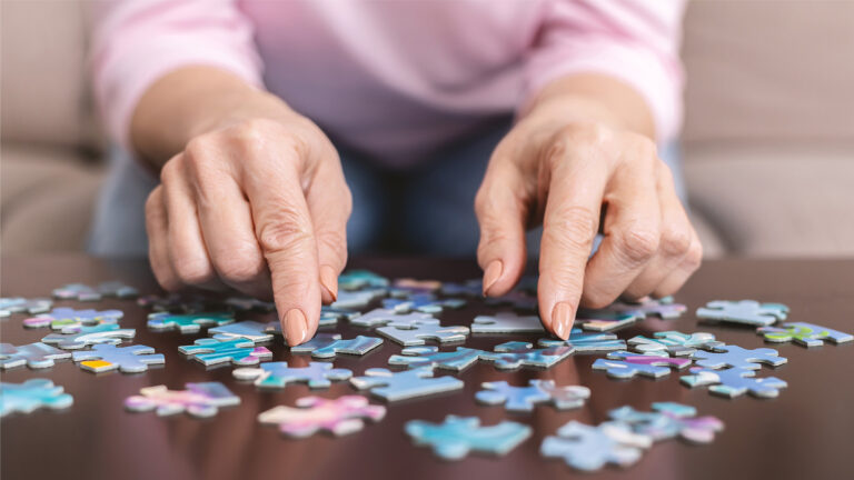 Eine ältere Person ordnet konzentriert bunte Puzzleteile auf einem Tisch an